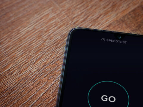 Lod, Israel - July 8, 2020: Speedtest app launch screen with logo on the display of a black mobile smartphone on wooden background. Top view flat lay with copy space.