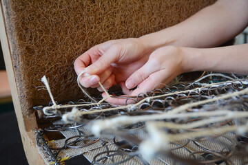 Woman fasten springs in upholstery workshop. Upholstery worker tying and sewing springs. Springs webbing, old chair restoration.