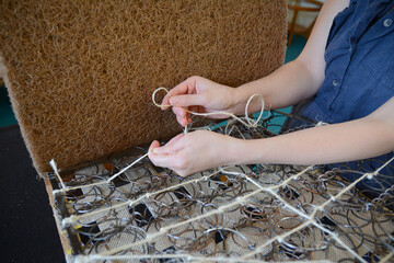 Woman fasten springs in upholstery workshop. Upholstery worker tying and sewing springs. Springs...