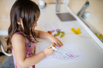 Little girl coloring a big leaf image on a paper sheet with a pen
