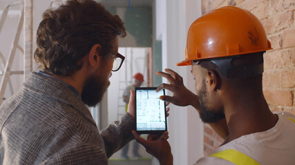 Back view of apartment owner and foreman discussing blueprint on digital tablet