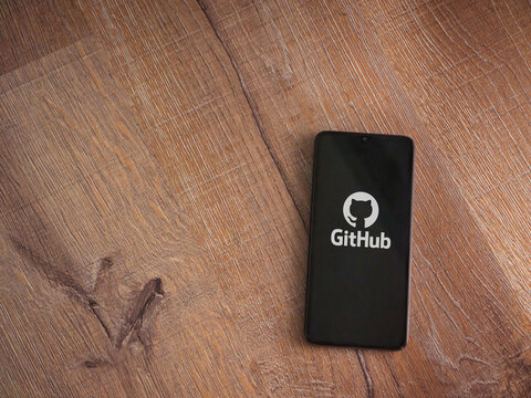 Lod, Israel - July 8, 2020: GitHub app launch screen with logo on the display of a black mobile smartphone on wooden background. Top view flat lay with copy space.