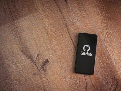 Lod, Israel - July 8, 2020: GitHub app launch screen with logo on the display of a black mobile smartphone on wooden background. Top view flat lay with copy space.