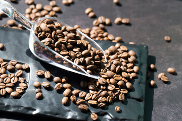 Fresh coffee beans in plastic scoop on black background.