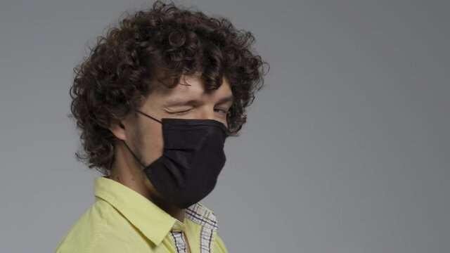 Curly man stands in a profile in a medical mask. Guy crossed his arms on his chest and turns discontentedly into the camera. High quality.