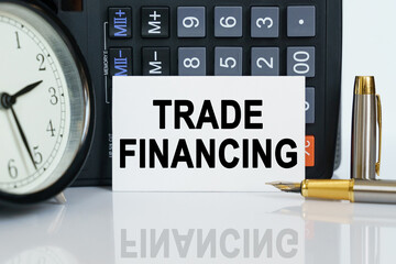 On the table there is a clock, a pen, a calculator and a business card on which the text is written - TRADE FINANCING