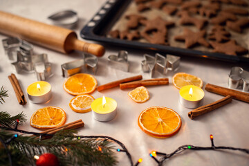 View of the table with white tablecloth, christmas decor, baking accessories and baking sheet with brown cookies. Winter holidays, festive mood, new year preparation.