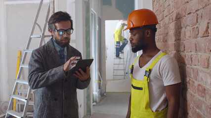 Worker and client using tablet pc at construction site planning renovation