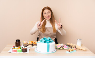 Obraz na płótnie Canvas Young redhead woman with a big cake smiling and showing victory sign