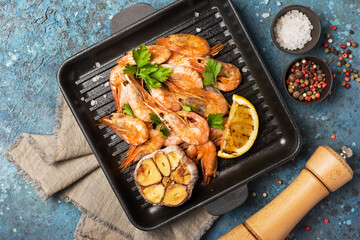Spicy fried shrimps on grill pan with lemon, garlic and green parsley