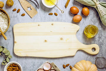 A wooden cutting board on a dark table surrounded by ingredients for baking a pie eggs, flour, honey, nuts, pumpkin, almonds. Top view, flat lay, copy space