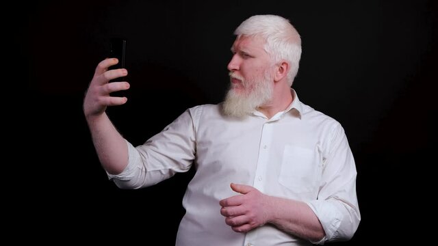 Funny man with albinism using phone and taking selfie, making faces on camera, isolated on black background.
