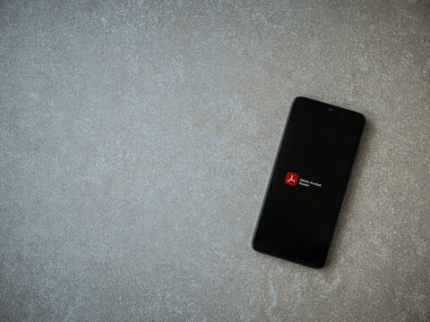 Lod, Israel - July 8, 2020: Adobe Acrobat Reader app launch screen with logo on the display of a black mobile smartphone on ceramic stone background. Top view flat lay with copy space.