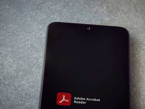 Lod, Israel - July 8, 2020: Adobe Acrobat Reader app launch screen with logo on the display of a black mobile smartphone on ceramic stone background. Top view flat lay with copy space.