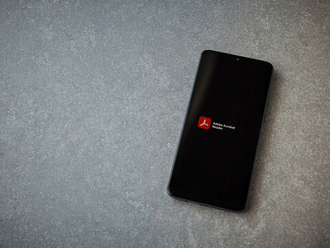 Lod, Israel - July 8, 2020: Adobe Acrobat Reader app launch screen with logo on the display of a black mobile smartphone on ceramic stone background. Top view flat lay with copy space.