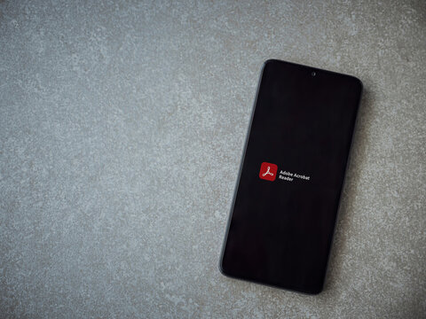 Lod, Israel - July 8, 2020: Adobe Acrobat Reader app launch screen with logo on the display of a black mobile smartphone on ceramic stone background. Top view flat lay with copy space.