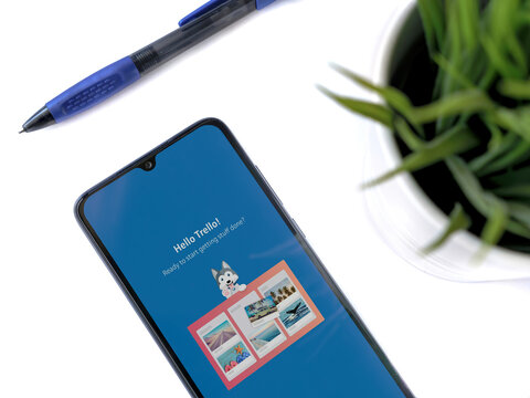 Lod, Israel - July 8, 2020: Modern minimalist office workspace with black mobile smartphone with Trello app launch screen with logo on white background. Top view flat lay with copy space.