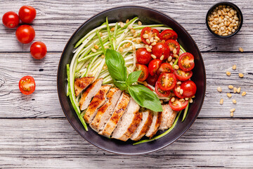 Fried chicken fillet and fresh vegetable salad of tomatoes, zucchini and pine nuts.