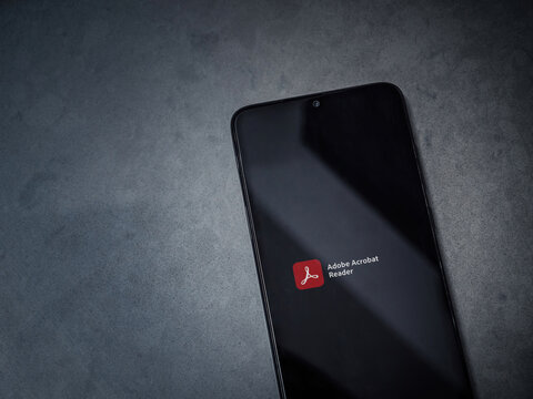 Lod, Israel - July 8, 2020: Adobe Acrobat Reader app launch screen with logo on the display of a black mobile smartphone on dark marble stone background. Top view flat lay with copy space.