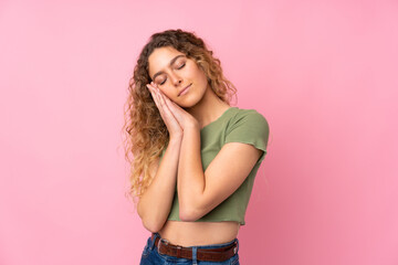 Young blonde woman with curly hair isolated on pink background making sleep gesture in dorable expression