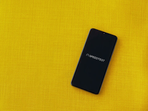 Lod, Israel - July 8, 2020: Speedtest app launch screen with logo on the display of a black mobile smartphone on a yellow fabric background. Top view flat lay with copy space.