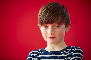 Portrait Of Young Boy Against Red Studio Background Smiling At Camera