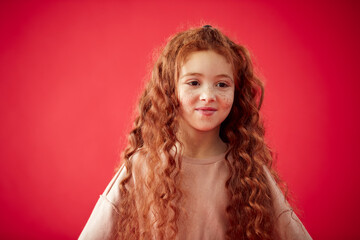 Portrait Of Girl With Long Red Hair Against Red Studio Background Smiling At Camera