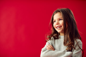 Portrait Of Young Girl With Folded Arms Against Red Studio Background Smiling At Camera