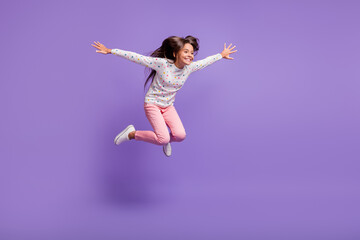 Full length body size photo little girl with long hair jumping high smiling happily isolated on bright violet color background