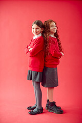 Two Elementary School Pupils Wearing Uniform Back To Back Against Red Studio Background