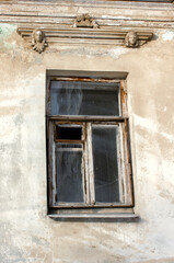 an antique window without shutters on a plastered wall decorated with stucco in the form of women's faces