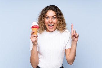 Young blonde woman with curly hair holding a cornet ice cream isolated on blue background pointing...