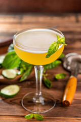 Gin-based citrus cocktail with cucumber and basil in a glass on a wooden background with basil leaves and slices of cucumber