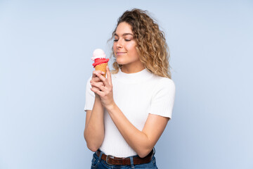 Young blonde woman with curly hair holding a cornet ice cream isolated on blue background