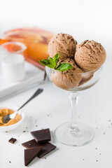 Balls of chocolate ice cream in a glass decorated with a sprig of mint and chocolate chips on a white background