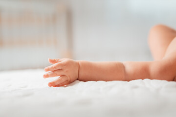 A hand of a baby lying on a white bed. Close-up of the arm. Copy space. Concept of parenthood and children's day