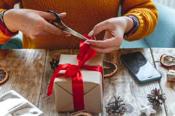 Young woman wrapping christmas present on table with new year deorations