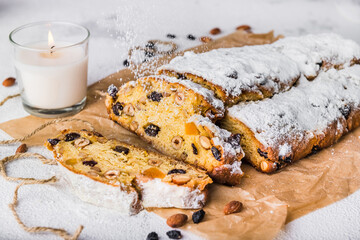 Christmas stollen with candied fruit and dried fruits on parchment on a white background with a white candle