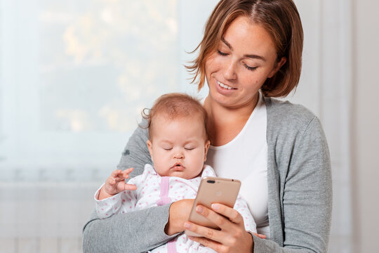 A mother holds a sleeping child in her arms and shows him something on her smartphone. Close-up portrait