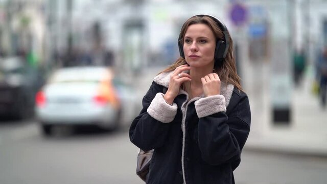 pretty sad adult woman is walking in big city with wireless headphones, listening love song and dreaming, portrait