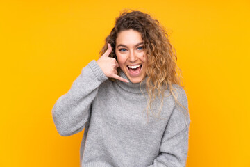 Young blonde woman with curly hair wearing a turtleneck sweater isolated on yellow background making phone gesture. Call me back sign