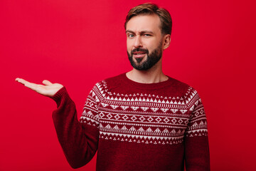 Curious handsome guy with brown beard posing in studio. Indoor shot of cheerful white man wears cozy knitted sweater.