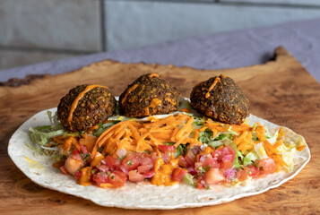 Wrap with falafal balls, colourful salad, with sauce over.