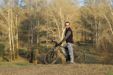 Sports brutal bearded guy on a modern mountain bike. Cyclist on the green hills in the spring.