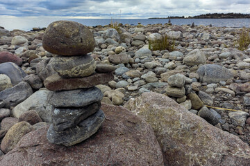 A meditation figure made of stones, folded on a large stone in the middle of a rocky beach overlooking the Ladoga islands on a cloudy day