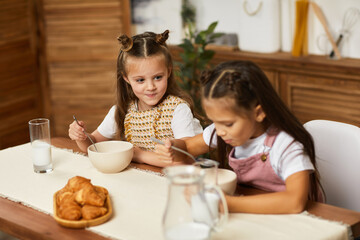 Obraz na płótnie Canvas happy little children girls friends having breakfast - fresh delicious croissants and milk in the kitchen.