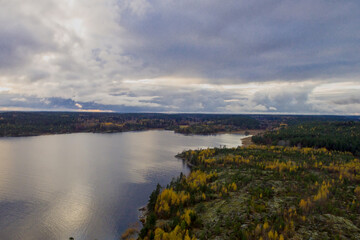 Rocky island with colorful autumn trees on Lake Ladoga and the sky reflected in the water