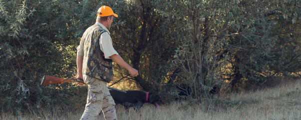 Duck hunter with shotgun walking through a meadow.