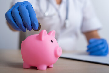 A faceless female doctor puts a coin in a piggy bank