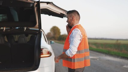 Electric car accident on the road. Man with reflective vest calling by phone about breakdown in her electric car assistance services, help repair. Emergency stop sign.